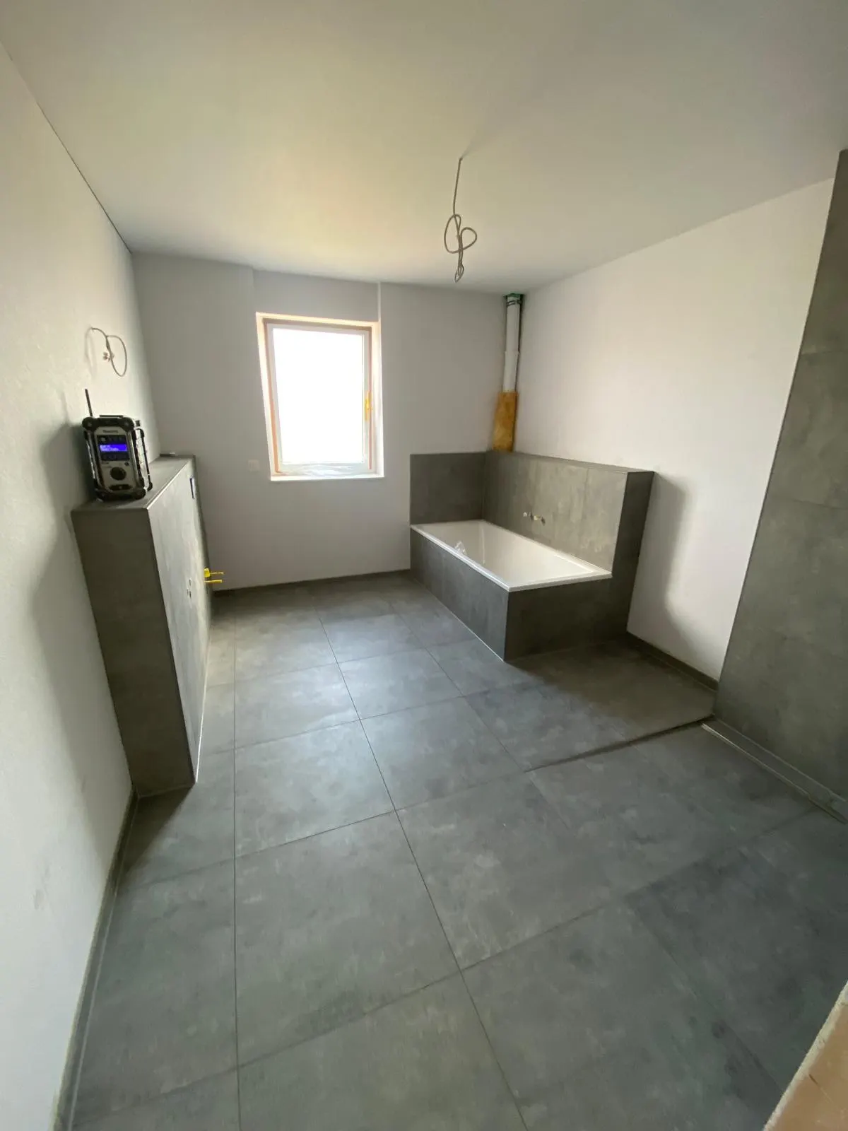 Badezimmer im Rohbau mit gefliester Wanne und Großformatfliesen